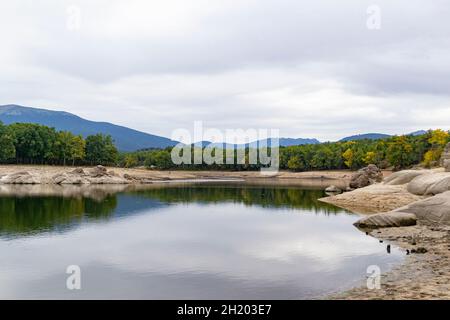 Blick auf einen Stausee, der die Landschaft im Wasser an einem bewölkten Tag in Segovia, in Castilla y León, in Spanien widerspiegelt. Europa. Horizontale Fotografie Stockfoto