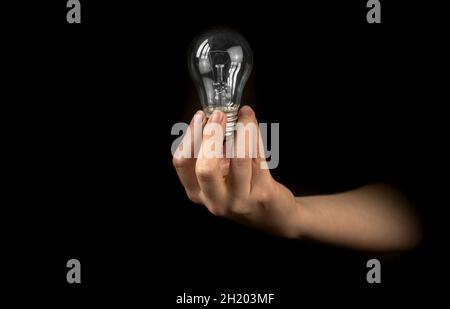 Hand der Frau mit Glühbirne auf schwarzem Hintergrund. Idee, Innovation, Denken und Inspiration für Geschäftskonzept Stockfoto