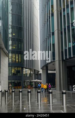 Eine Gruppe von Touristen, die an einem nassen Oktobertag zwischen Bürogebäuden in der Lime Street in der City of London, England, spazieren. Stockfoto