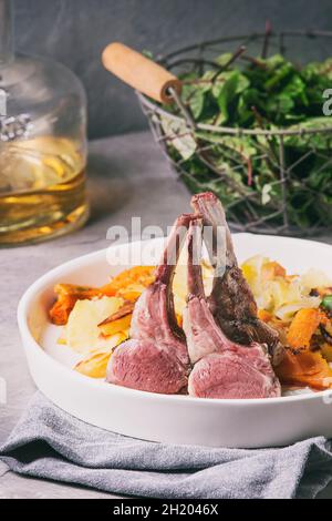 Sous Vide Lammkarree mit Sauce und hintergrünem Süßkartoffel in Keramikplatte mit grünem Salat und Weißwein serviert Stockfoto