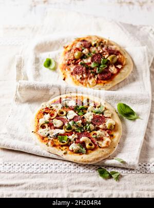 Zwei rustikale Pizzas mit Chorizo, grünen Oliven und Basilikumblättern Stockfoto
