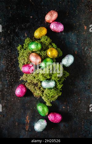 Schokoladeneier, die in helle Folie eingewickelt sind und ein Osternest umgeben Stockfoto