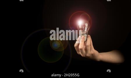 Hand einer Frau mit beleuchteter Glühbirne auf schwarzem Hintergrund. Idee, Innovation, Denken und Inspiration für Geschäftskonzept Stockfoto