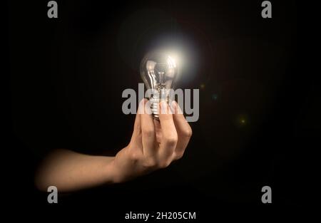 Glühbirne in der Hand der Frau auf schwarzem Hintergrund. Neue Idee oder Inspirationskonzept Stockfoto