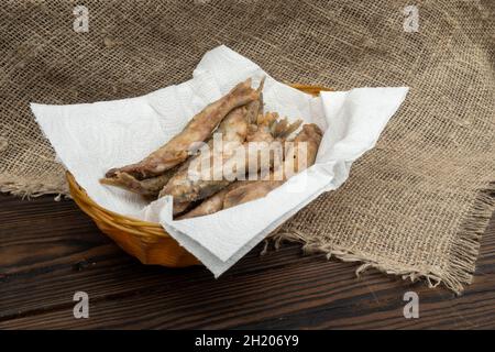 Gebratener Fisch auf einer Papierserviette in einem Korbkorb auf einem Holztisch Stockfoto