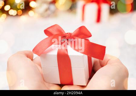 Weihnachts-Geschenkbox mit roter Schleife in Frauenhand auf dem Hintergrund von Weihnachtsbaum und Schnee Stockfoto