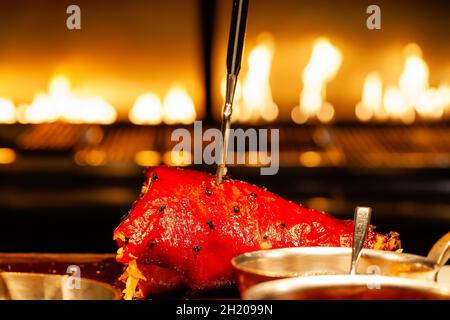 Gebratenes rotes Schweinebein mit Gewürzen, Pfeffer, Fleischgabel in moderner Restaurantküche Stockfoto