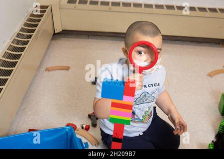 Bildung Vorschule 3-4-Jähriger Junge mit Lupe auf Turm er baute aus bunten Kunststoff Verbindungsbriken zu sehen (Duplo) Stockfoto