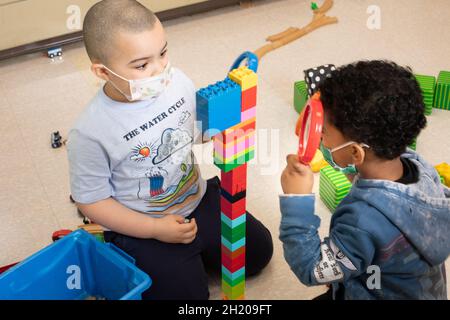 Bildung Vorschule 3-4-Jährige zwei Jungen, die im Blockbereich spielen, einer mit einer Lupe, um den farbenfrohen Turm zu betrachten, den sie aus Verbindungsflächen bauten Stockfoto