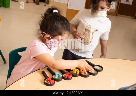 Bildung Vorschule 3-4-Jährige zwei Mädchen, die mit einer Lupe spielen, ein Mädchen, das hölzerne Alapabet-Buchstaben auf jede Lupenlinie legt Stockfoto