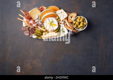 Verschiedene Käsesorten auf Holzbrettteller, Oliven, Trauben, Brot auf schwarzem Stein-Hintergrund, Draufsicht, flaches Lay, Kopierraum. Stockfoto
