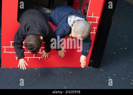 Bildung Vorschule 3-4-Jährige zwei Jungen, die sich über den Rand der Spielgeräte lehnen, um sich die Hände auf die Oberfläche zu schlagen Stockfoto