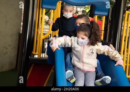 Bildung Kindergarten Spielplatz Kinder spielen auf der Rutsche mit Gesichtsmaske zum Schutz vor Covid-19 Stockfoto