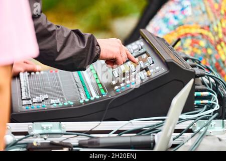 Toningenieur, der den Audiomischer bei Live-Konzerten im Freien manuell justiert, Schieberegler und Tasten auf dem Schreibtisch des Audiomischpults. Professioneller Bühnensound-Mixer bei Stockfoto
