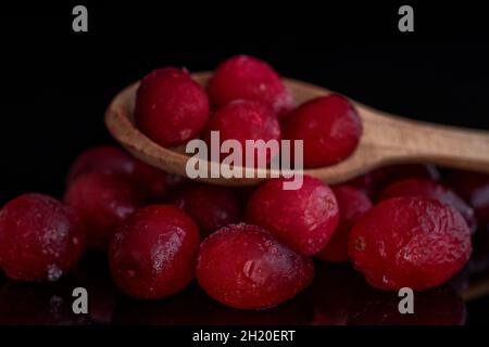 Mehrere gefrorene Preiselbeeren mit einem Löffel aus Holz, Nahaufnahme, isoliert auf schwarz. Stockfoto