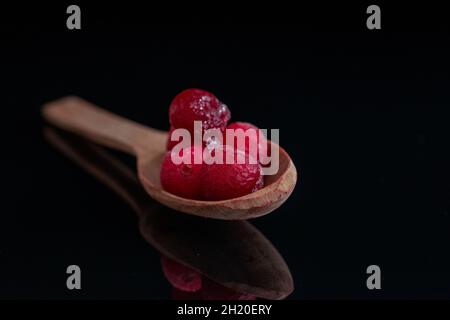 Mehrere gefrorene Preiselbeeren mit einem Löffel aus Holz, Nahaufnahme, isoliert auf schwarz. Stockfoto