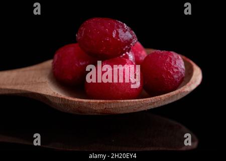 Mehrere gefrorene Preiselbeeren mit einem Löffel aus Holz, Nahaufnahme, isoliert auf schwarz. Stockfoto