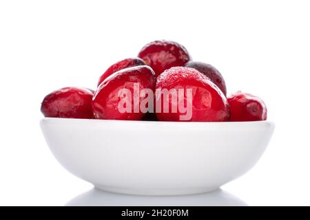 Mehrere Beeren von roten frisch gefrorenen Cranberries in einer weißen Keramikschale, Nahaufnahme, isoliert auf Weiß. Stockfoto