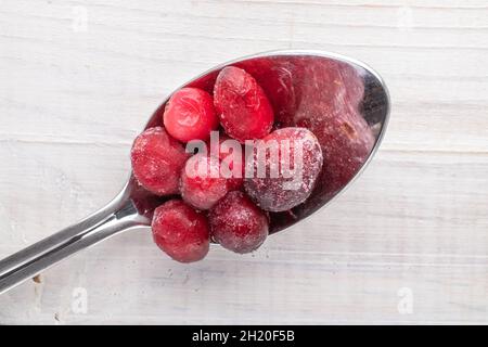 Frisch gefrorene rote Bio-Preiselbeeren mit einem Metalllöffel, auf einem Holztisch, Nahaufnahme, Draufsicht. Stockfoto