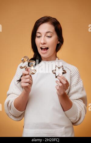 Frau in Überraschung hält Weihnachts-Ausstecher auf gelbem Hintergrund. Stockfoto