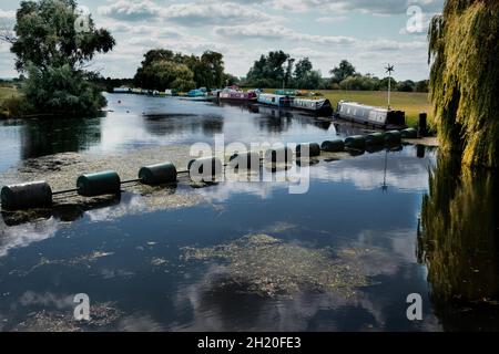 Bottisham Schleuse und Wehrschutzbarriere auf der River Cam mit Schmalbooten, die am Flussufer in Cambridgeshire England festgemacht sind Stockfoto