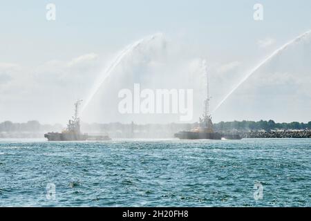 Schwimmende Schlepper sprühen Wasserstrahlen und demonstrieren die Brandbekämpfung mit Wasserwerfern. Löschboote sprühen Schaum mit Löschschläuchen. Offshore-Stützschiff Stockfoto