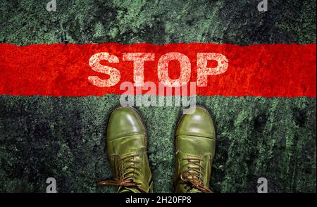 Das Wort "Stop" auf dem Asphalt vor deinen Füßen in grünen Stiefeln. Blick von oben. Stopplinie. Stockfoto