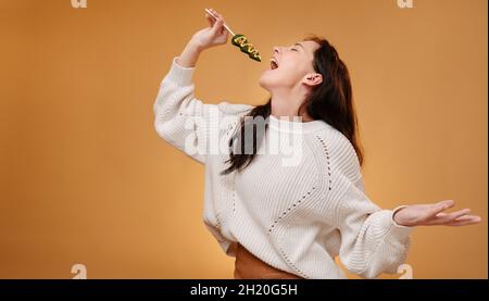 Frau in einem weißen Pullover singt in einen Weihnachtsbaum-Lollipop. Stockfoto