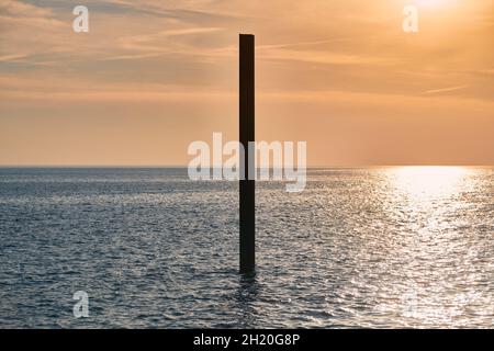 Große, rostige Stahlbausäule im blauen Meer mit ruhigen Wellen bei Sonnenuntergang, Sonnenlicht, das sich auf die Meerwasseroberfläche reflektiert. Vertikal verlassene Gebäudeteil Stockfoto