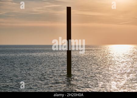 Große, rostige Stahlbausäule im blauen Meer mit ruhigen Wellen bei Sonnenuntergang, Sonnenlicht, das sich auf die Meerwasseroberfläche reflektiert. Vertikal verlassene Gebäudeteil Stockfoto