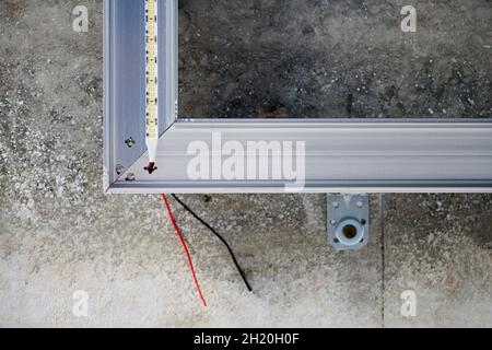 LED-Streifen mit Aluminiumprofil an rauer Wand. Betondecke mit LED-Beleuchtung im Wohngebäude, Innenfoto, Nahaufnahme. Renovierung des Hauses Stockfoto