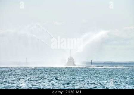 Schwimmende Schlepper sprühen Wasserstrahlen und demonstrieren die Brandbekämpfung mit Wasserwerfern. Löschboote sprühen Schaum mit Löschschläuchen. Offshore-Stützschiff Stockfoto