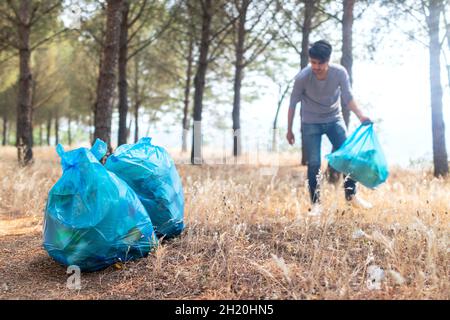 Freiwilliger Mann sammelt Plastikmüll unter Kiefern. Selektiver Fokus. Stockfoto