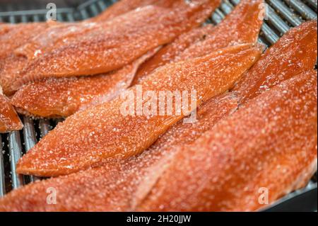 Auf dem Förderband liegen viele Stücke Rotfischfilet. Der Fisch ist mit einer Schicht groben Salzes bedeckt Stockfoto