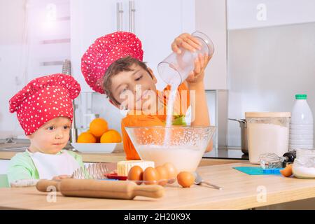 Jungen, die im Kochhut kochen, geben Zucker in die Rührschüssel Stockfoto