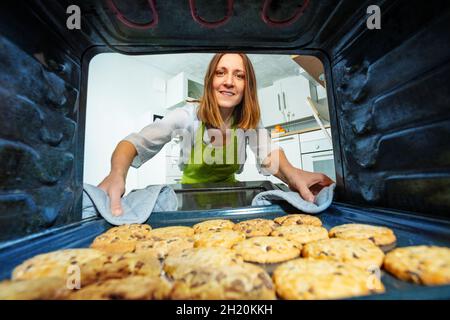 Frau nimmt Tablett mit gebackenen Plätzchen aus dem Ofen Stockfoto