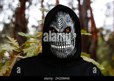 Nahaufnahme des grimmigen Reaper. Mann in Todesmaske mit Feuerflamme in den Augen auf Natur Eichenwald Blätter Hintergrund. Faschingskostüm, gruselige Zähne. Ha Stockfoto