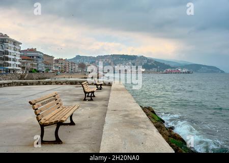 Hölzerne Sitzbank in Guzelyali, Bursa, Türkei bei regnerischem und bewölktem Wetter. Mudanya Meer und Menge Leute auf dem Weg in der Küste zu Fuß. Stockfoto