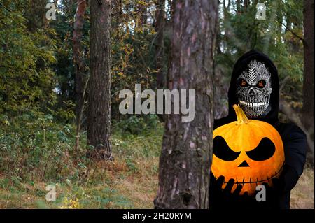 Grimmiger Schnitter hält halloween Kürbis Kopf. Mann in Todesmaske wi Stockfoto