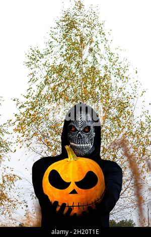 Nahaufnahme des grimmigen Reaper. Mann in Totenmaske mit Feuerflamme in den Augen auf gelbem Birkengrund. Faschingskostüm, gruselige Zähne. Halloween Stockfoto