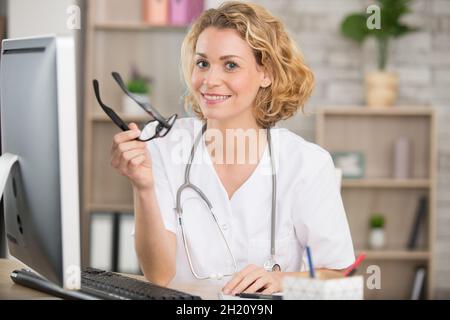 Die Ärztin saß am Computertisch und hielt eine Brille Stockfoto