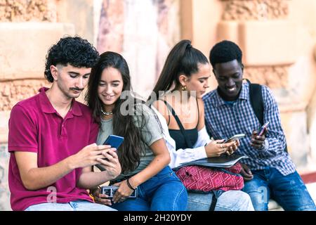Freunde verschiedener Ethnien nutzen das mobile Sitzen im Freien Stockfoto