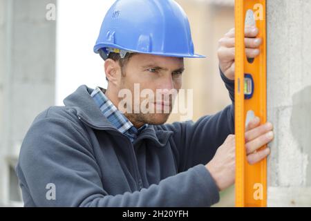 baumeister vor Ort, überprüft Außenwand mit Wasserwaage Stockfoto