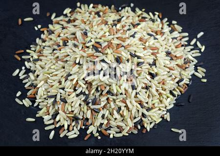 Reishaufen, gemischt aus verschiedenen Sorten auf einer schwarzen Tafel. Eine Mischung aus rohem, parboiled und wildem Reis. Reisbeere, Schwarzer Jasmin, Roter Jasmin, Braun Stockfoto