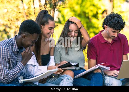 Eine Gruppe von Studenten, die Notebooks lesen und einen Laptop im Freien benutzen Stockfoto