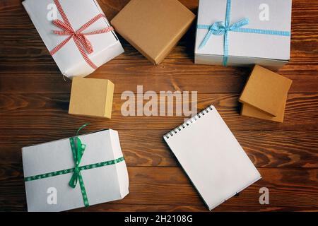 Flache Verlegung von leerem Notizbuch und Geschenkboxen auf Holztischhintergrund. Platz für jedes Design kopieren. Weihnachtsneujahr und andere Feiertage Konzept. Raum für moderne kreative Arbeit eines Designers. Stockfoto