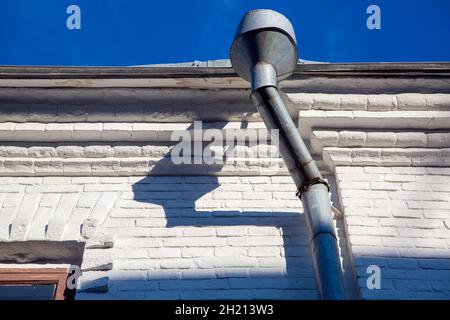Eine Regenrinne eines verzinkten Sturmablaufrohrs an den Vorsprüngen eines Gebäudes mit einer weißen Fassade aus weißen Ziegeln an einem sonnigen, klaren Tag. Stockfoto