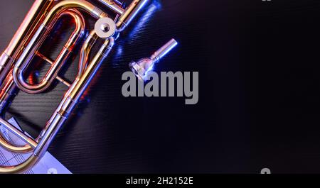 Jazz-Posaune mit leeren Laken, beleuchtet mit farbigen Lichtern auf schwarzem Tisch. Draufsicht. Horizontale Zusammensetzung. Stockfoto