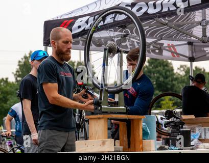 Columbus, OH USA 08-07-2021: Ein kaukasischer Mann mit Ingwerbart fixiert die Reifenausrichtung eines Fahrrads in einer Outdoor-Werkstatt mit einem Radtrichtungsständer. Bild Stockfoto