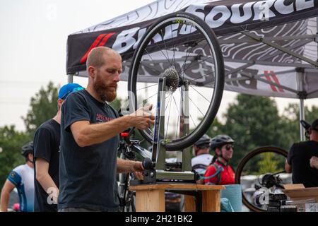 Columbus, OH USA 08-07-2021: Ein junger kaukasischer Mechaniker verwendet einen Radruderständer, um ein Fahrradrad während einer Outdoor-Veranstaltung zu fixieren und auszurichten. c Stockfoto